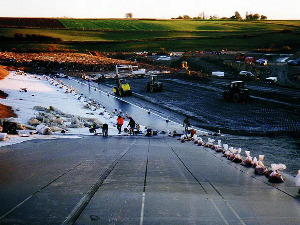 Instalación de geomembrana sobre terreno preparado en una obra de contención.